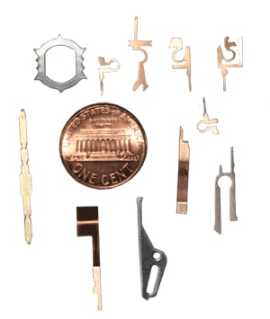 Small stamped copper, brass and steel contacts next to a penny for scale